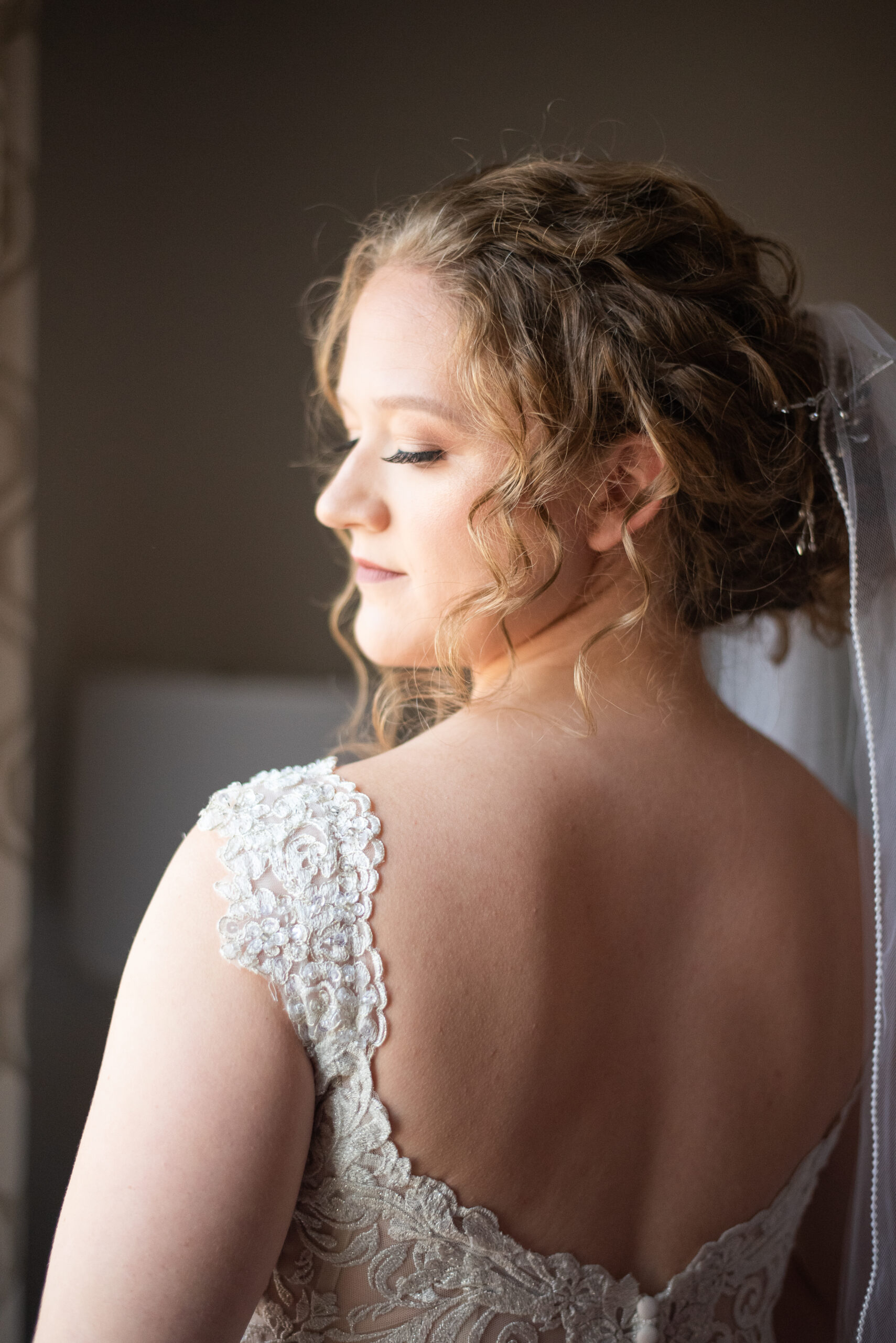 bride in a lace wedding gown looking over her shoulder out the window