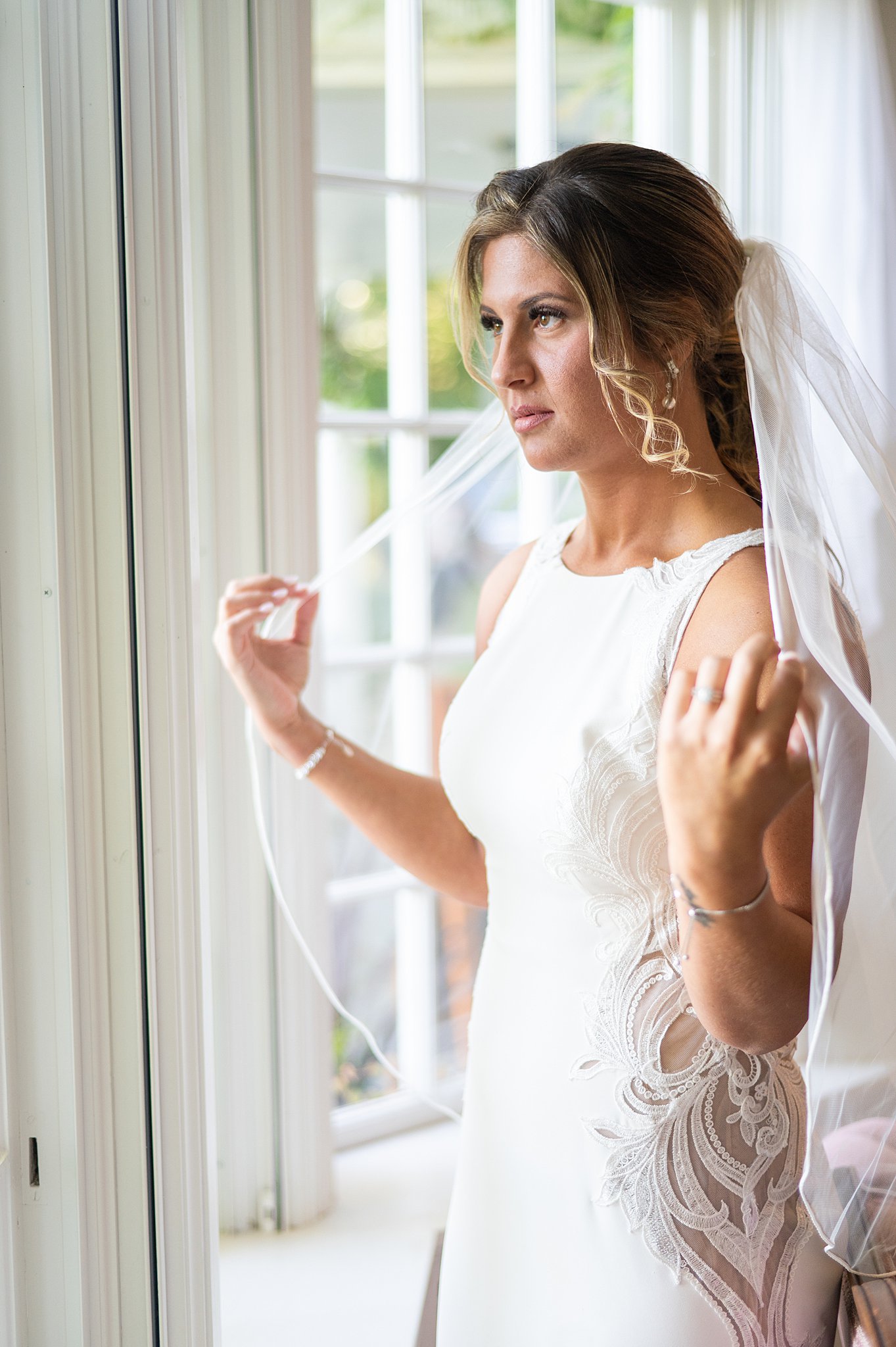 bride standing at a window with her hands on her veil at her asa waters mansion wedding
