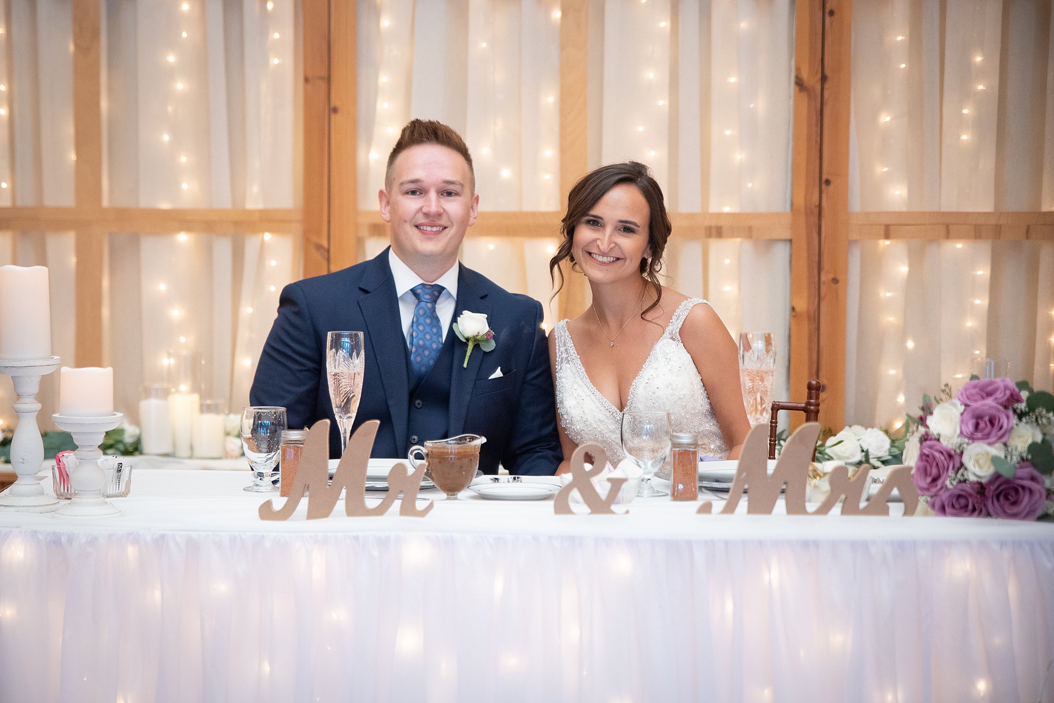bride and groom sit at their table decorated with flower and lights